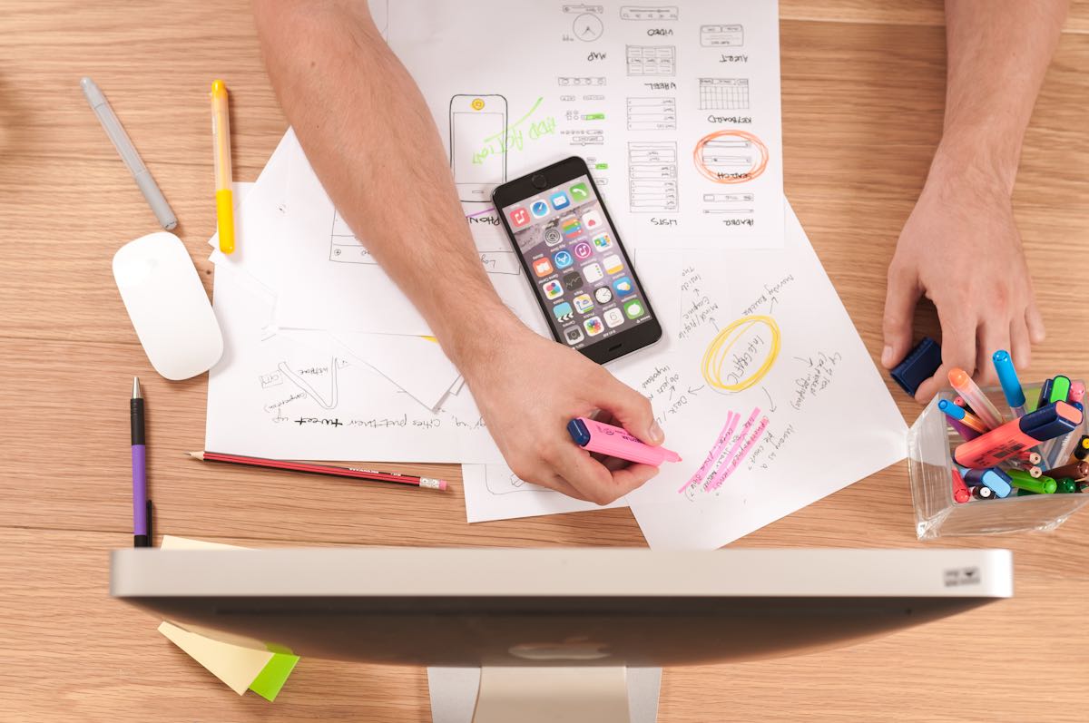 Overhead view of a desk with a smartphone, wireframe sketches, and colourful planning notes for a social media strategy